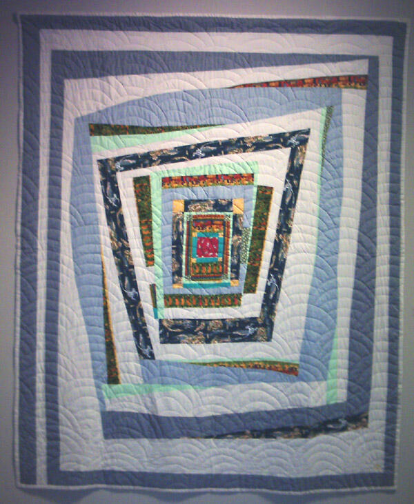 A large blue and white quilt with a spiral pattern. It has yellowish and brown colors in the middle. The actually quilting pattern is in the shape of a wave.